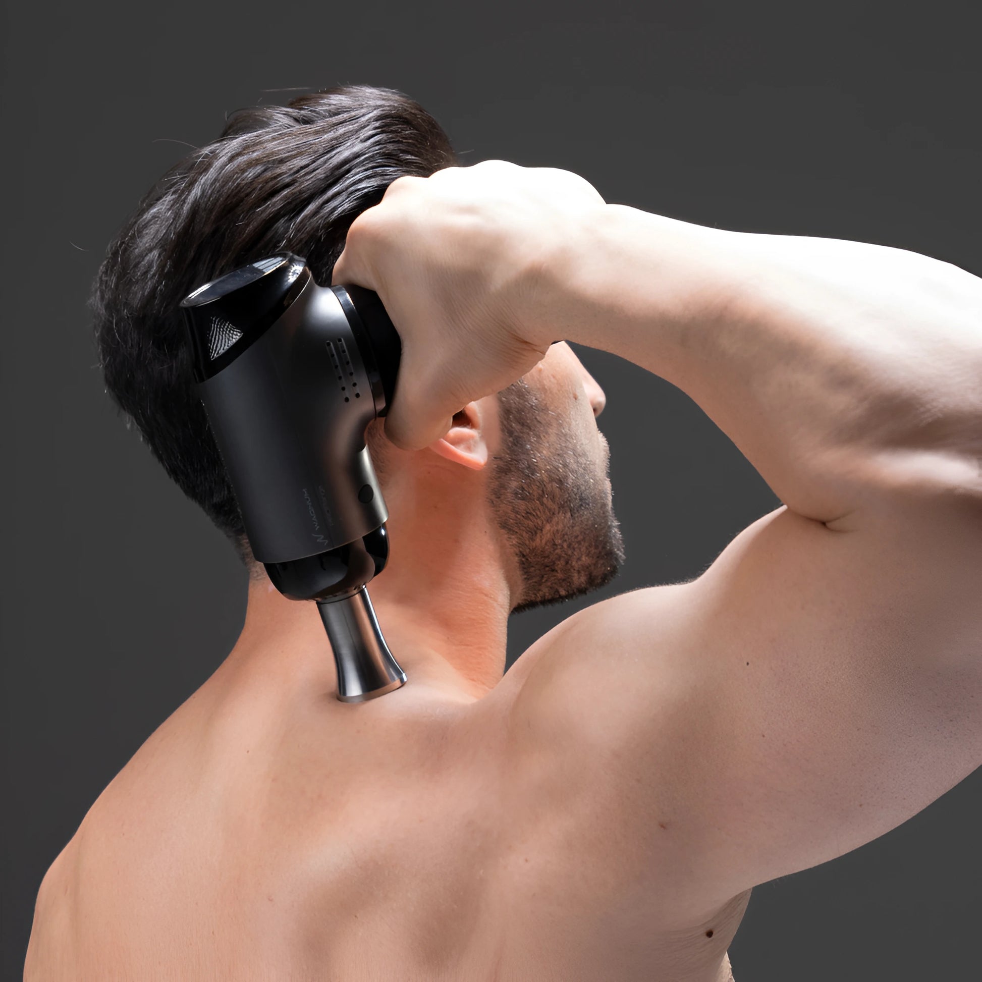 A man using a WAGNUM ProRange massage gun on his neck against a dark background.