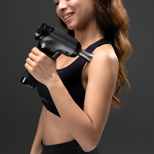 Woman using WAGNUM PRORange massage gun against a dark background.